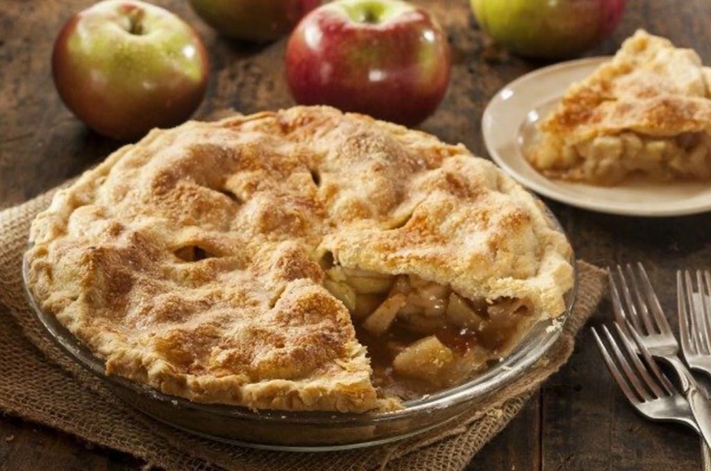 Warm apple pie sitting on a table with a slice cut out
