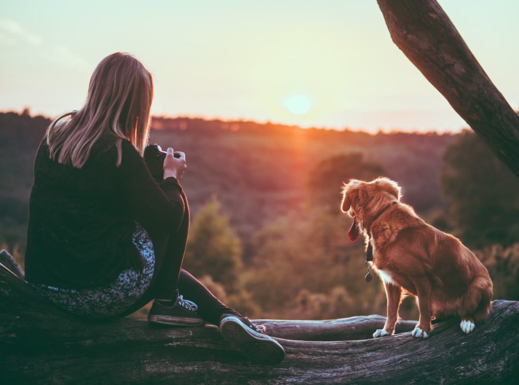 Woman sitting with her dog in front of a sun set