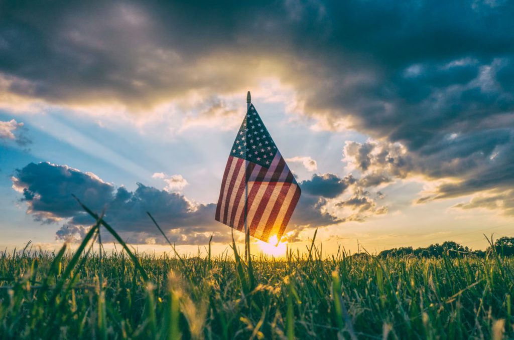 American flag sticking out of the grass with a beautiful sunset in the background