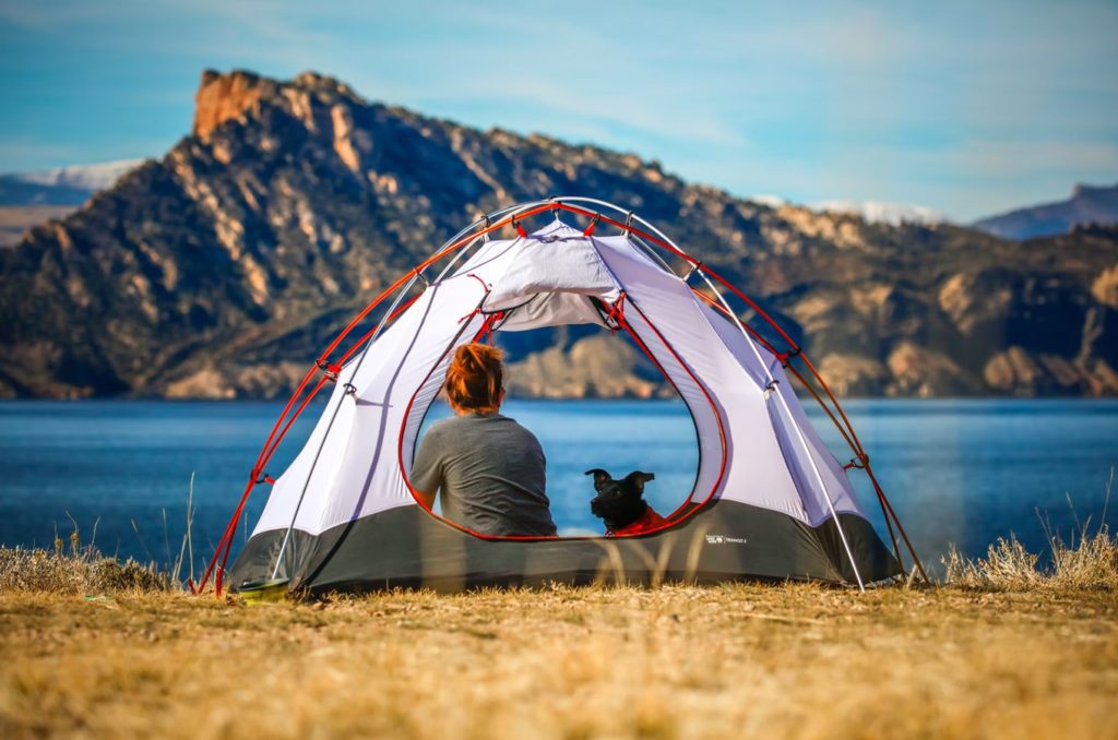 Woman sitting in her tent with her black dog while camping next to a lake