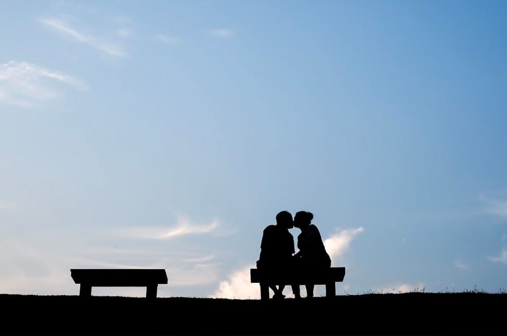 A man and woman on a date while kissing and sitting on a bench in lake Chelan