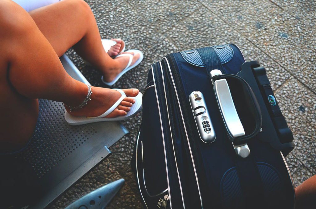 Downward image of a woman sitting on a bench nect to her packed suitcase