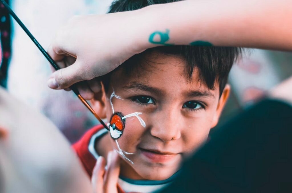 Boy getting a Pokemon ball painted on his face for Halloween