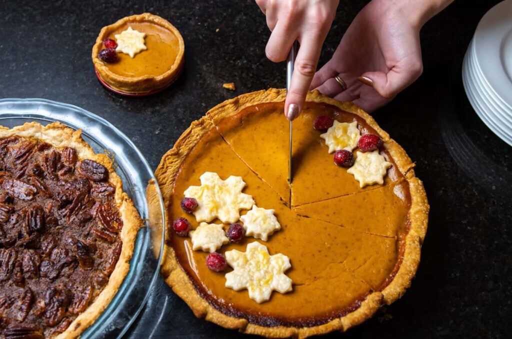 Woman's hand slicing a piece of pumpkin pie during Thanksgiving