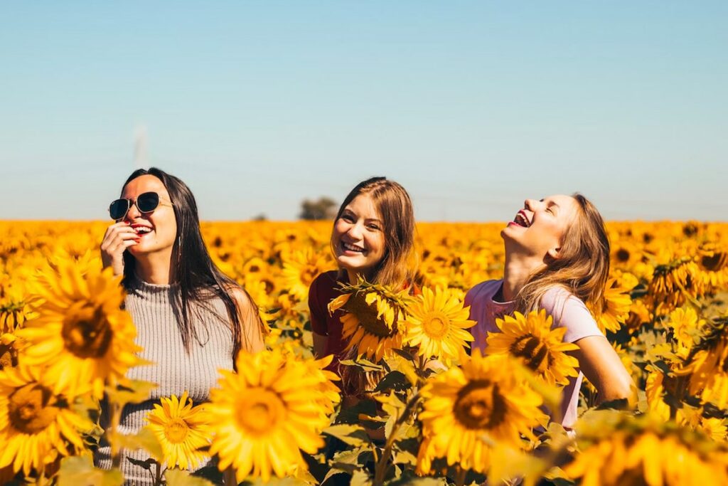 Three woman laughing in a field of sunflowers during their transformational travel to Lake Chelan